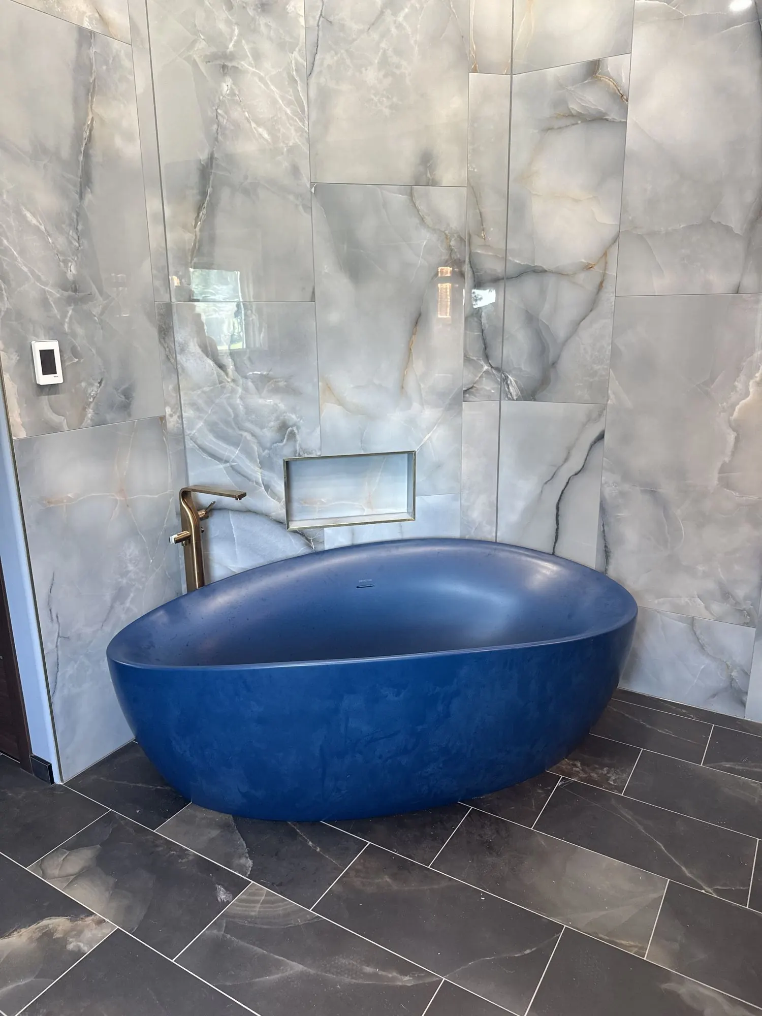 Primary bathroom remodel in Liberty, MO with freestanding blue soaking tub and marble slab walls Primary bathroom remodel in Liberty, MO with freestanding blue soaking tub and marble slab walls